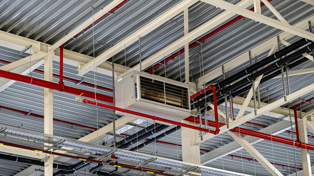 Rode ventilatiekanalen en leidingwerk aan het plafond van een bedrijfshal
